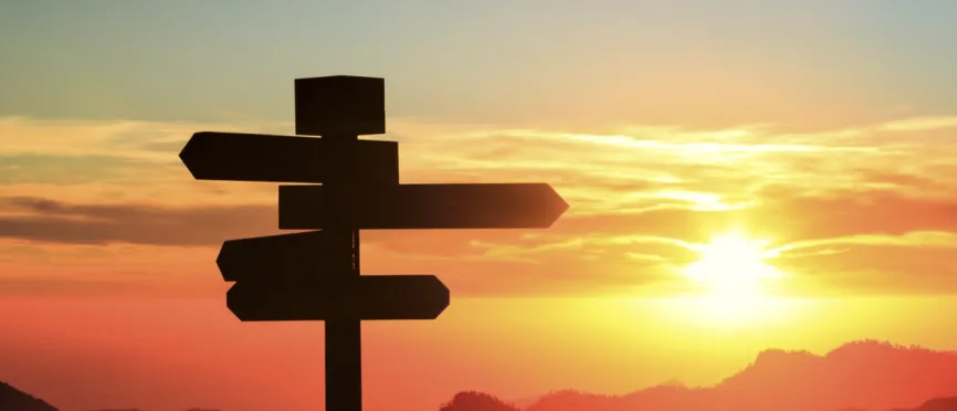 Silhouette of a sign with four directions with mountains and sunset in the background