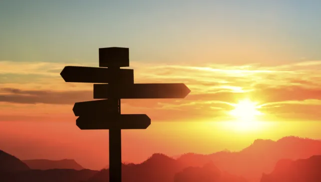 Silhouette of a sign with four directions with mountains and sunset in the background